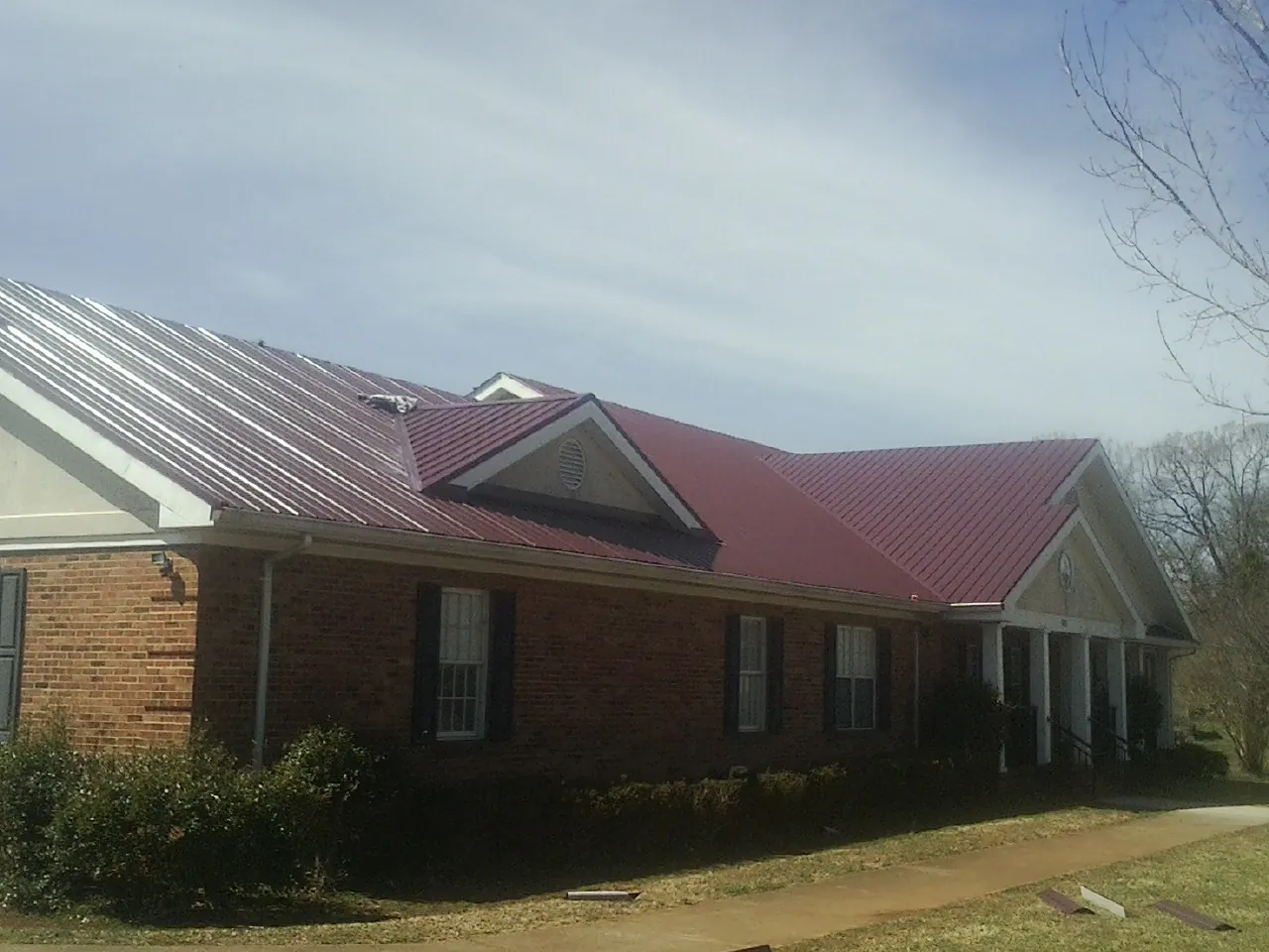 Red metal roof with gabled entries on a long brick building, from a Hail Damage Roof Repair job in Bucyrus