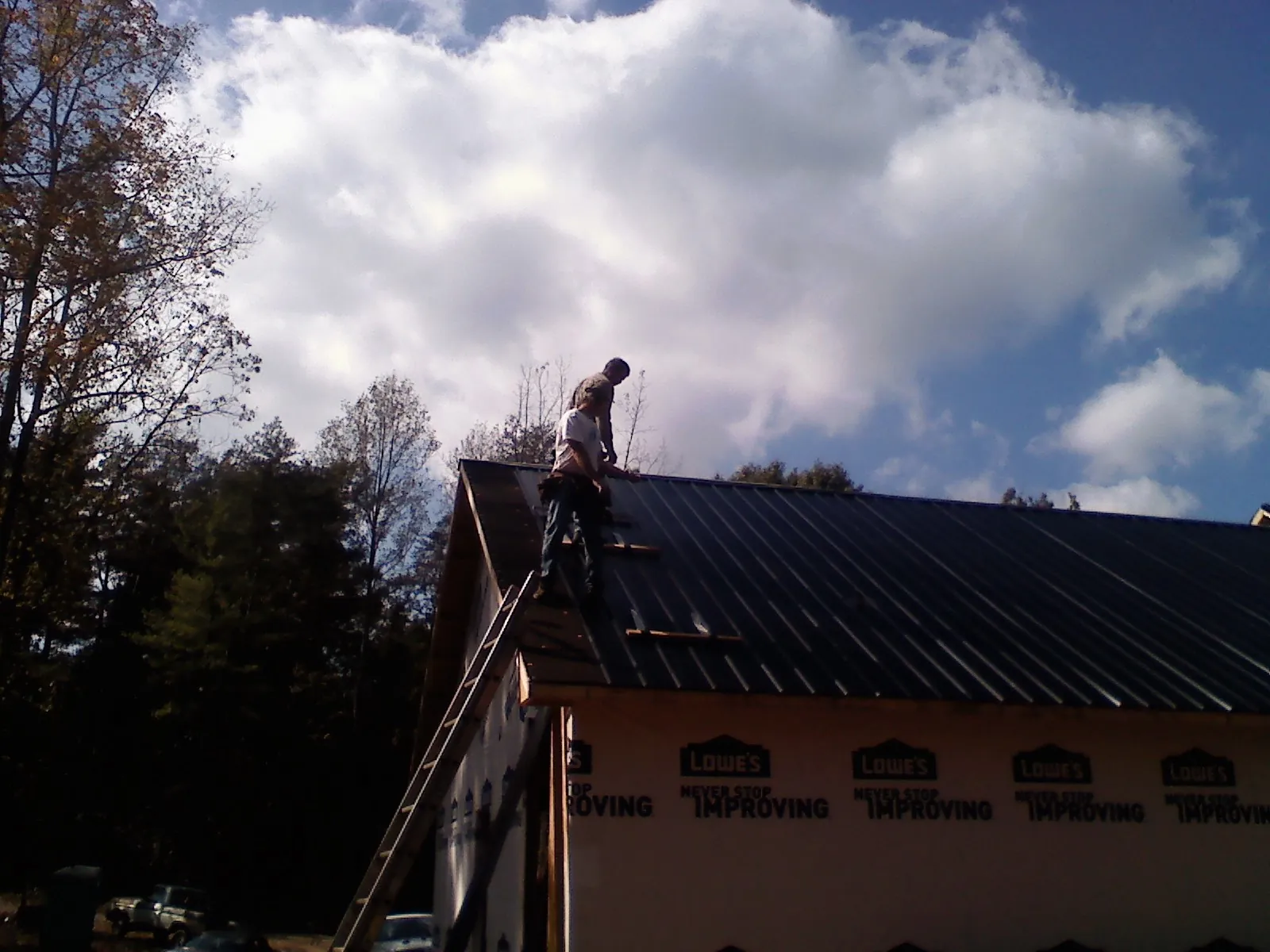 Roofer fastening dark metal panels high against a cloudy sky, from a Roof Inspection job in Bucyrus