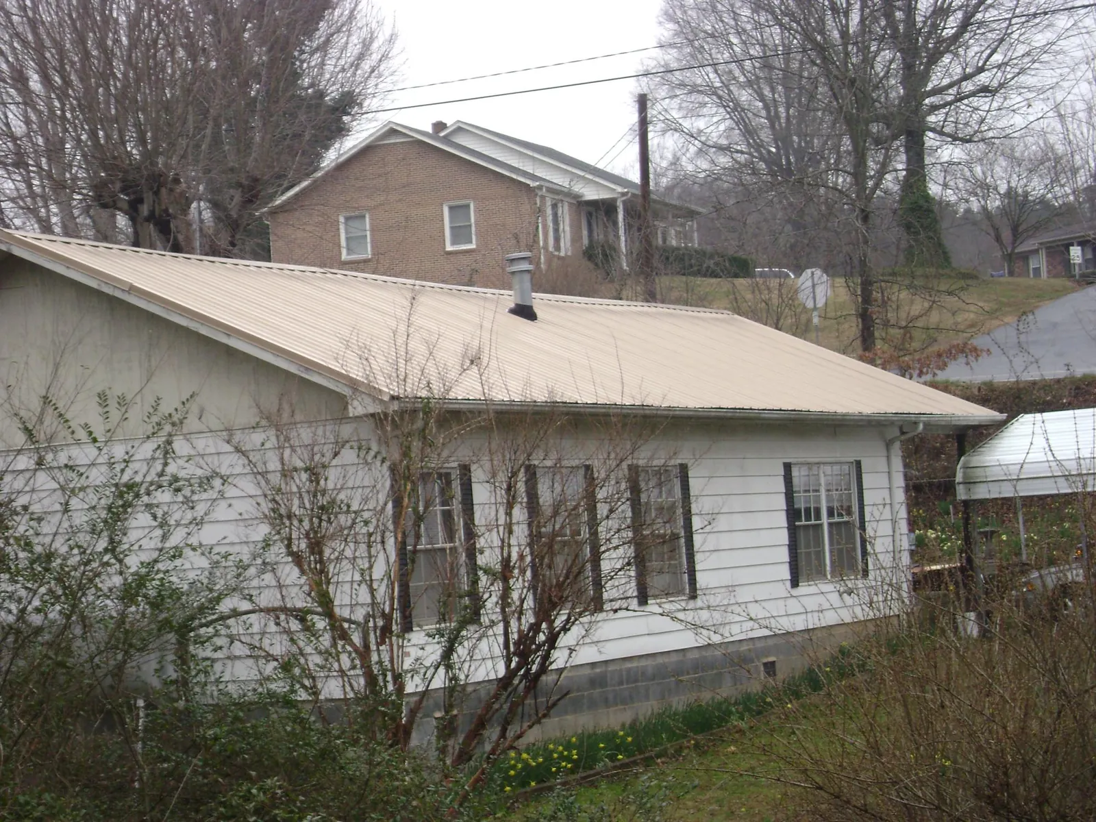Tan metal roof on a white sided house set into a hillside — Commercial Roofing by Roofing Brothers in Bucyrus